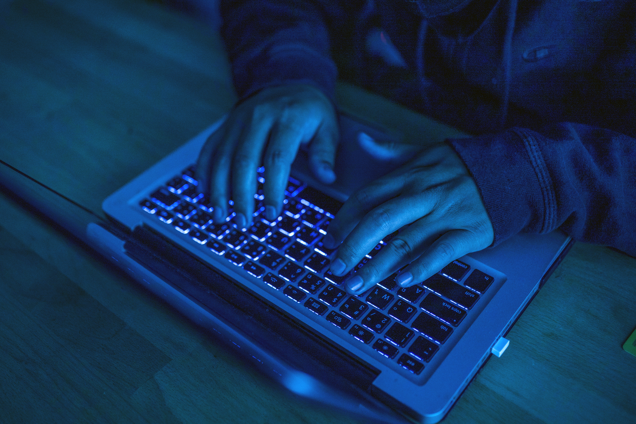 Person typing on a laptop keyboard under dim lighting