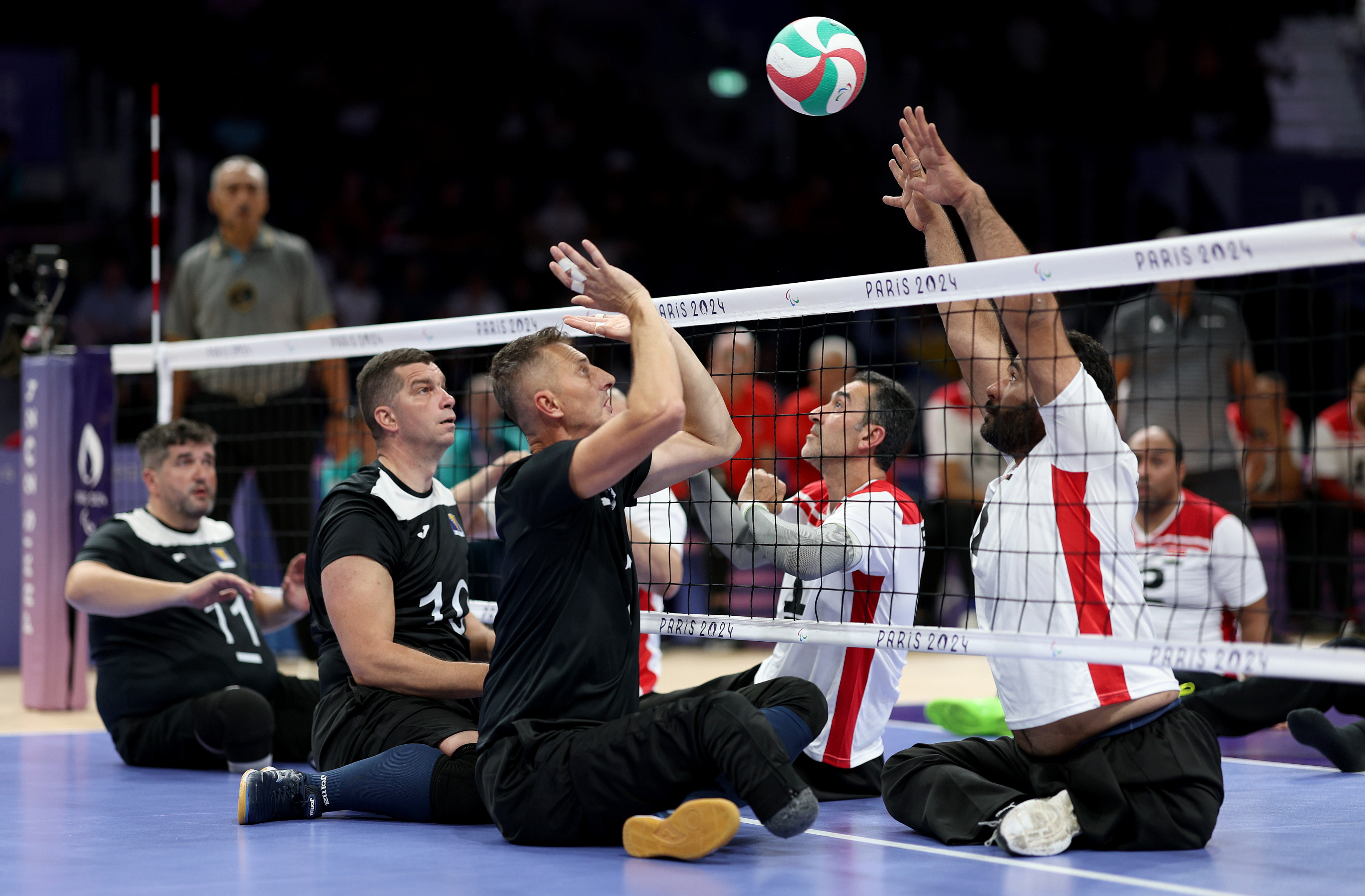Paralympic sitting volleyball match, players from opposing teams in action reaching for the ball