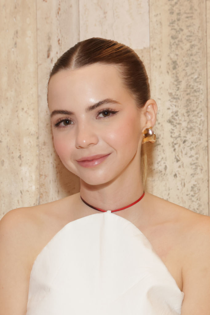 Bobbi Althoff is wearing a strapless dress and earrings, with her hair in a sleek updo, smiling for the camera at an event