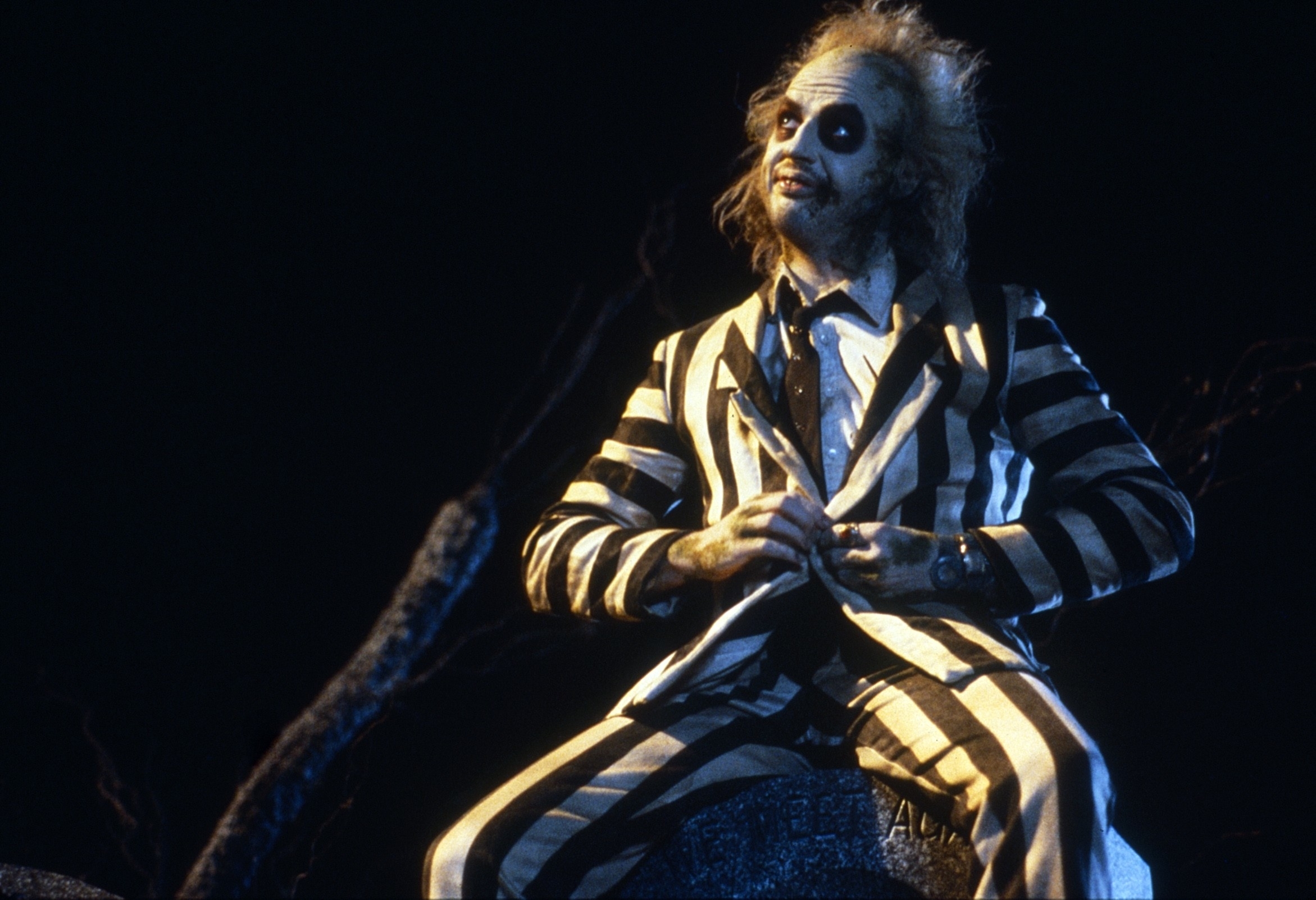Michael Keaton as Beetlejuice, wearing a black-and-white striped suit with disheveled hair and pale facial makeup