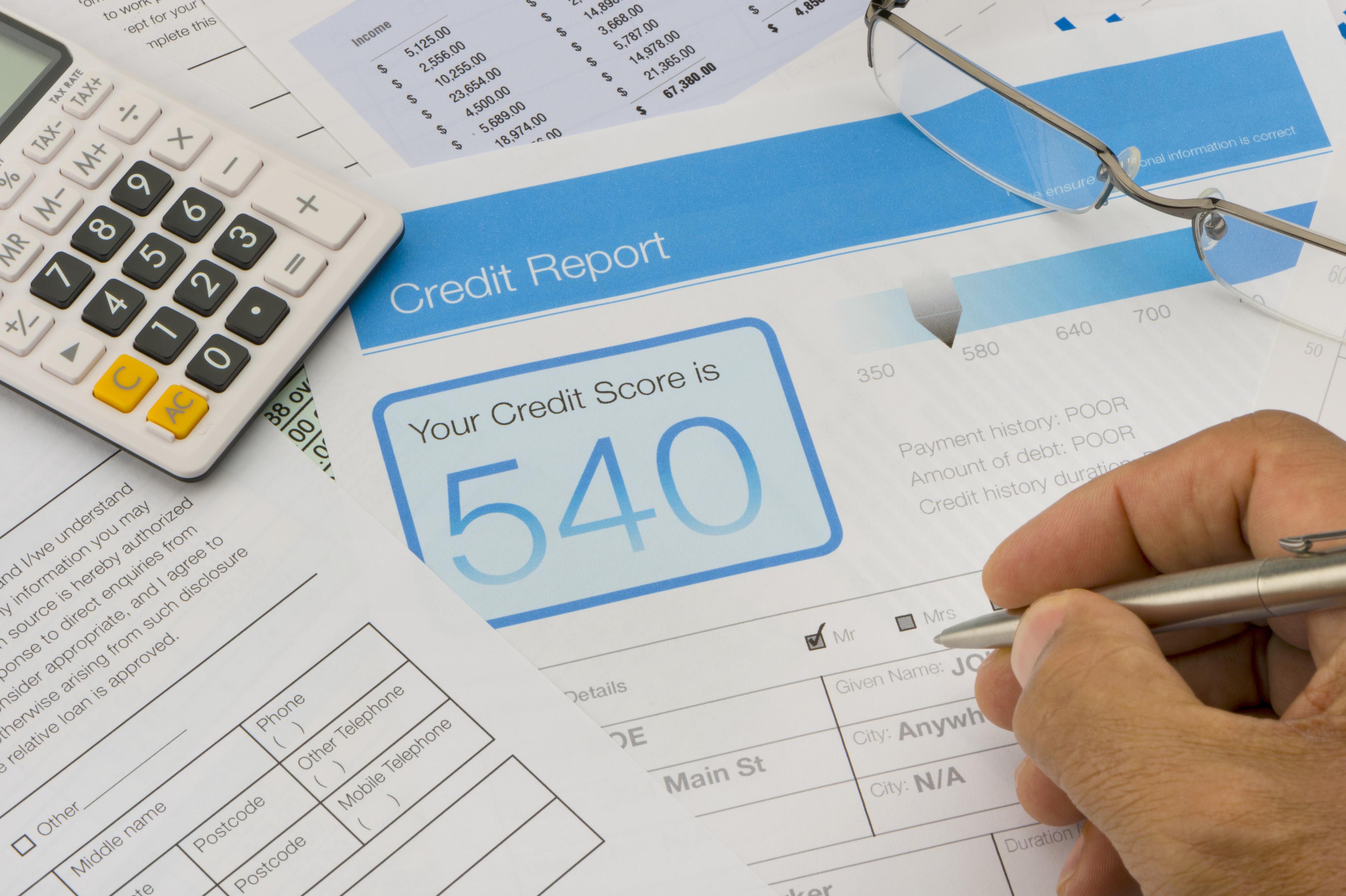 A credit report with a highlighted score of 540 is shown. Nearby are a calculator, glasses, and a hand holding a pen, filling out a form