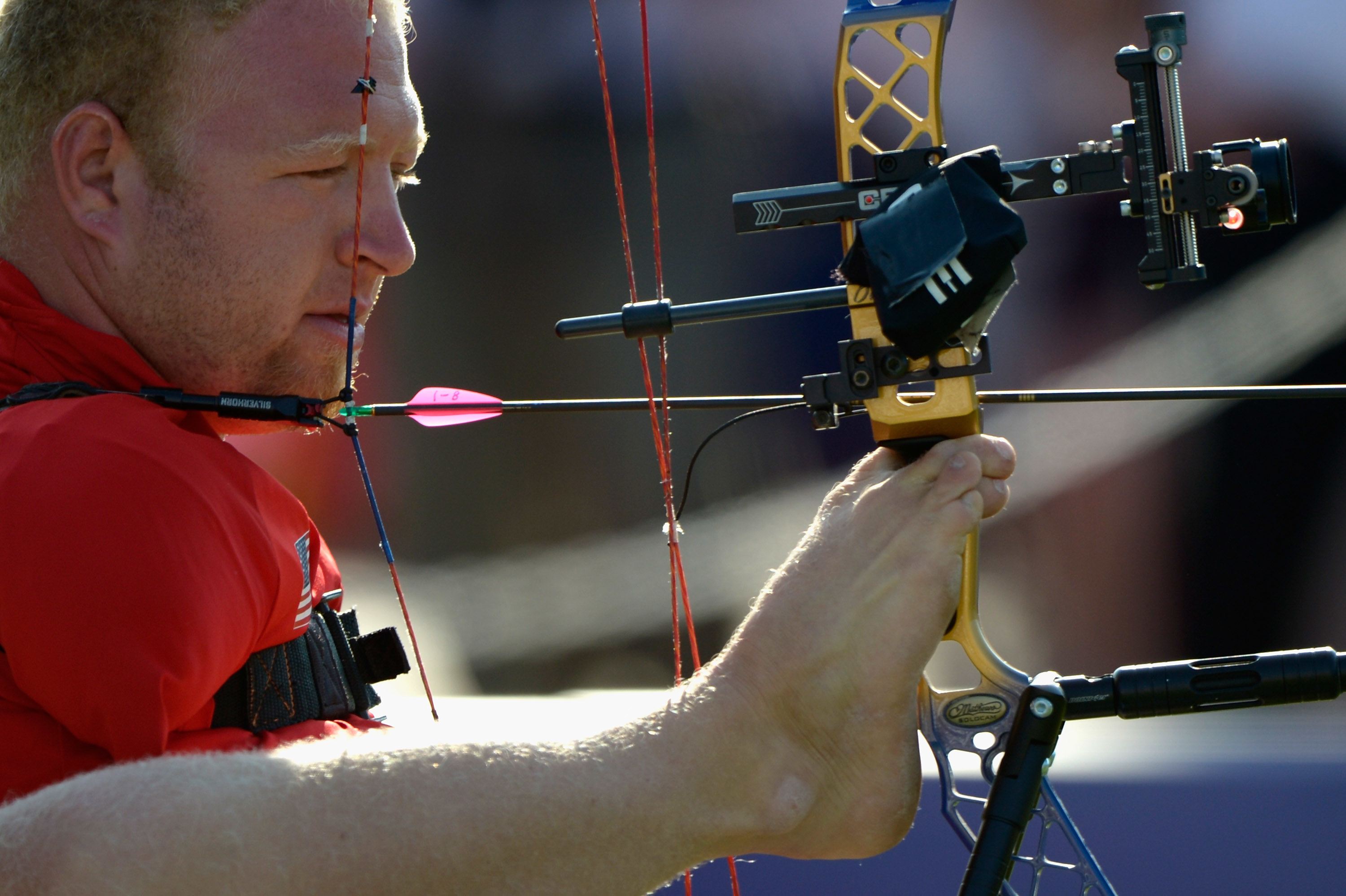 Man with no arms pulling back a bowstring with his foot, focused on aiming the arrow