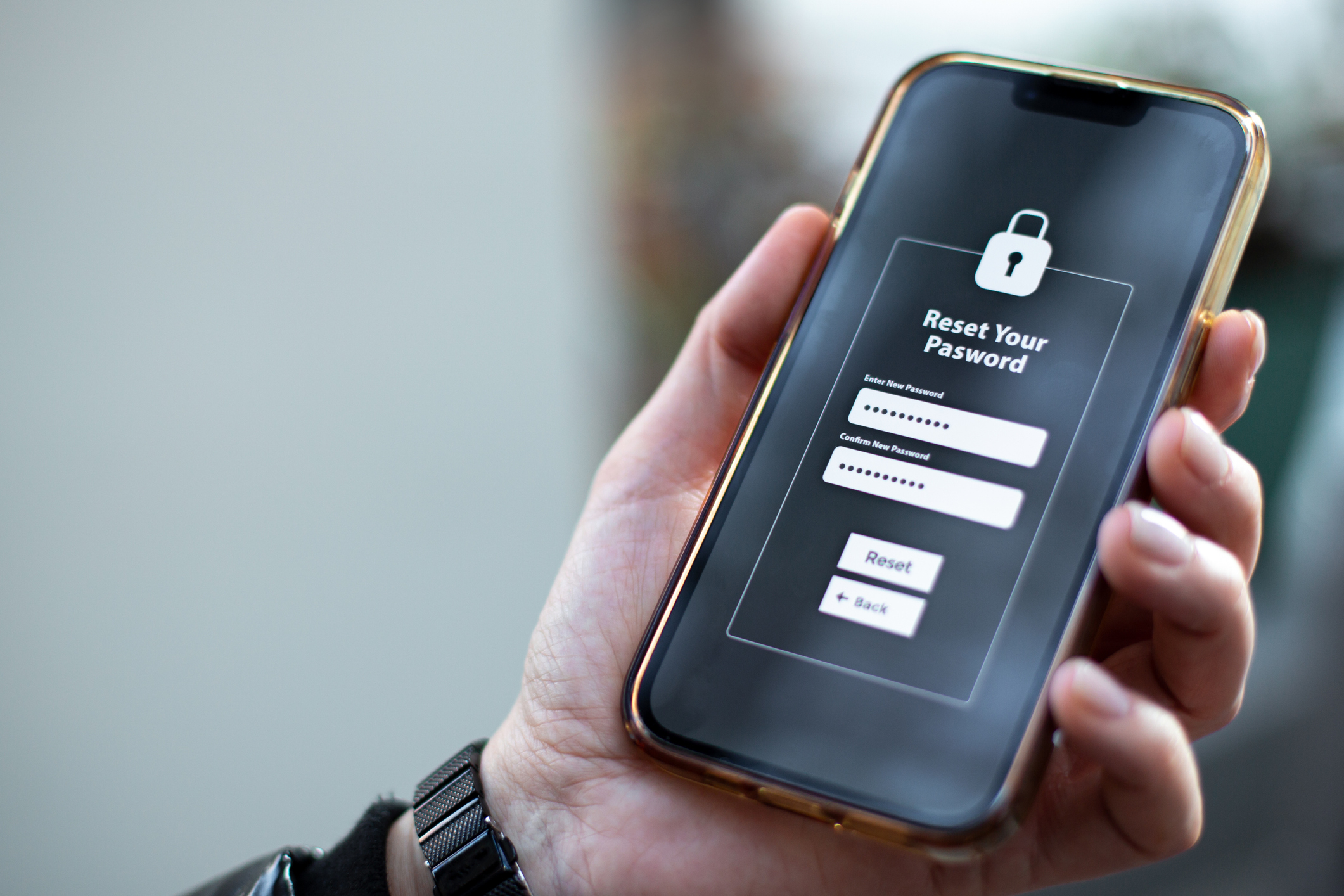 A person holds a smartphone displaying a password reset screen, showing fields for the current password and new password, with &quot;Reset&quot; and &quot;Back&quot; buttons