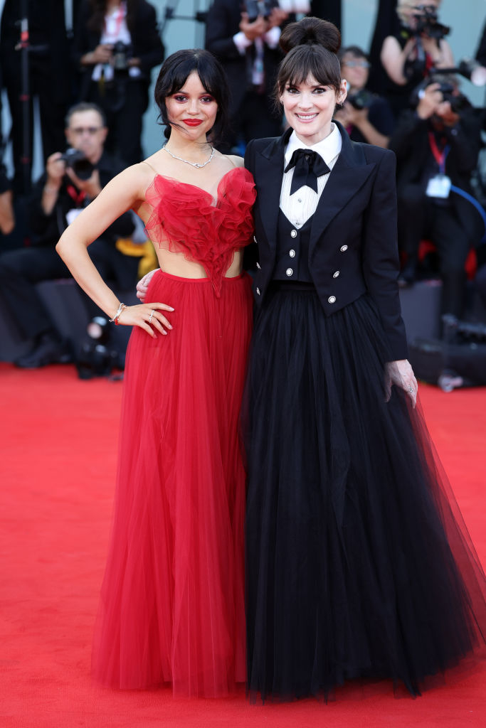 Jenna Ortega in a heart-shaped bodice gown and Winona Ryder in a dark tuxedo-style gown with bowtie at a red carpet event