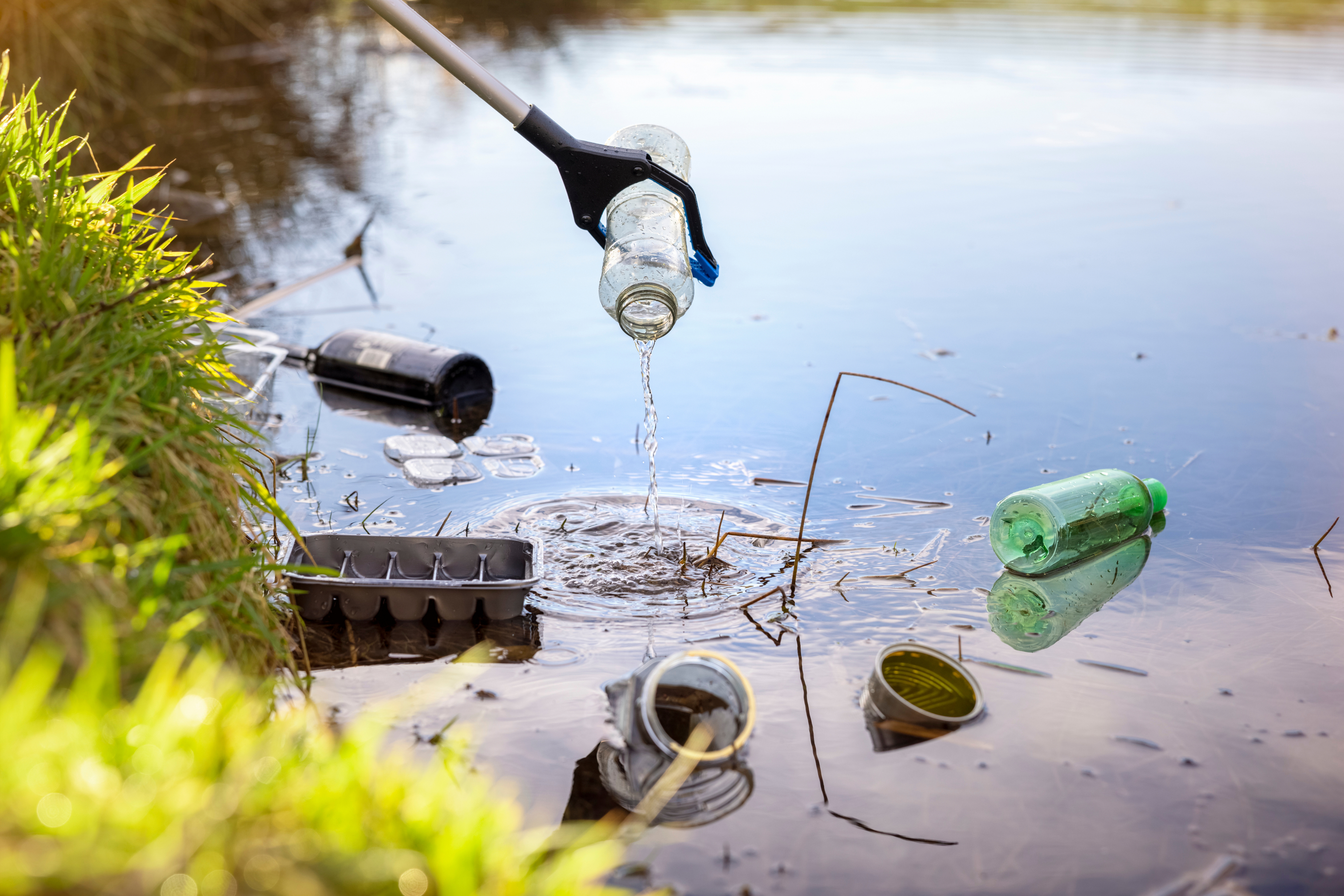 A person using a grabber tool to clean up litter from a pond, removing bottles and other trash
