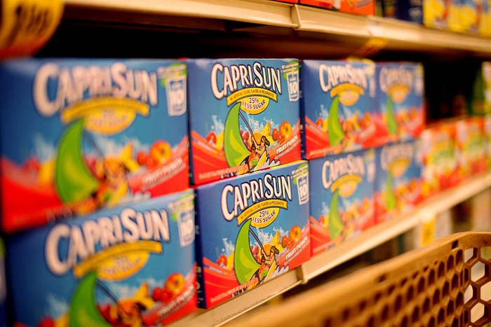 Capri Sun juice boxes displayed on a supermarket shelf, showcasing packages with fruit illustrations and a playful design