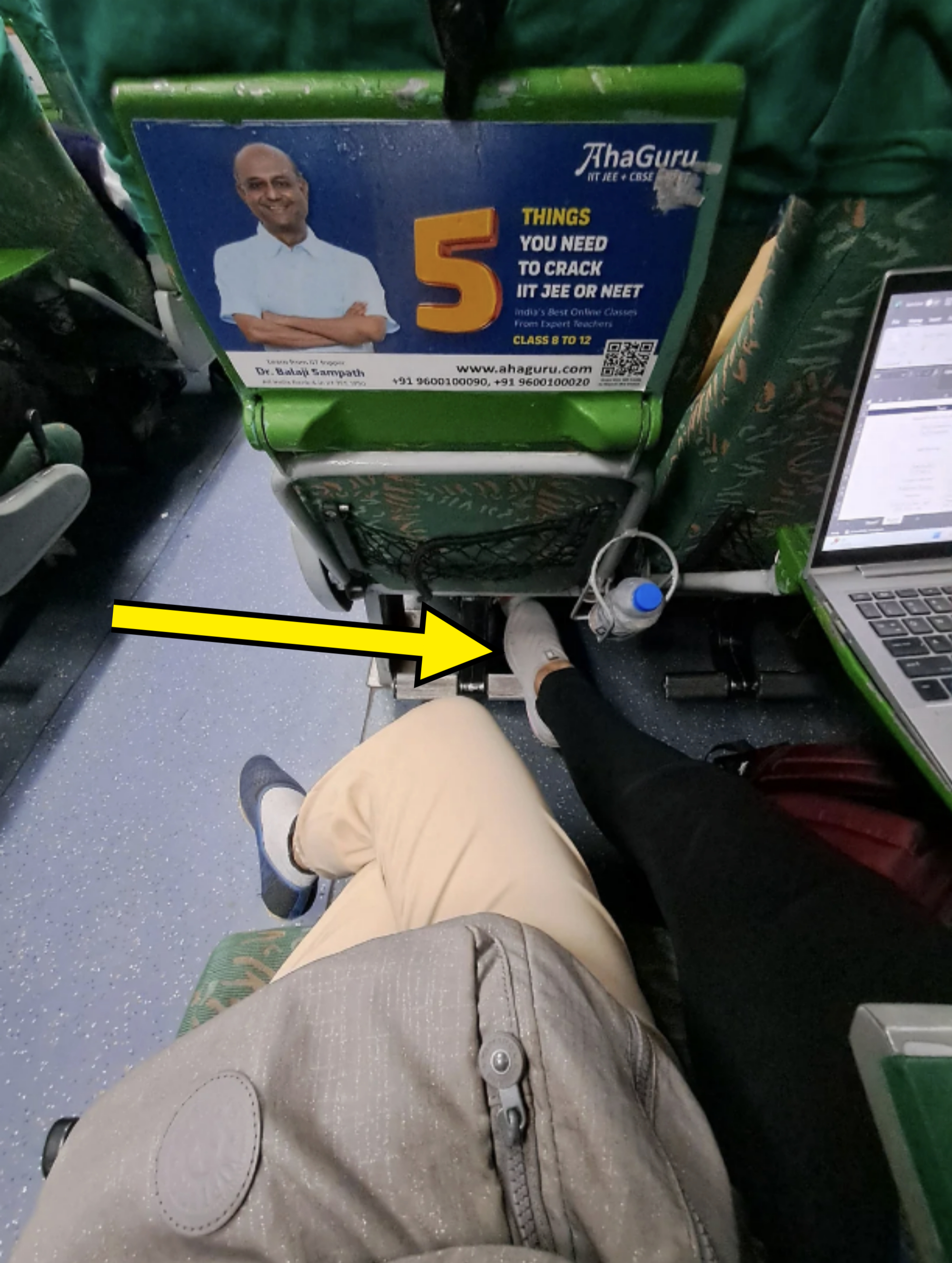 Two people seated, one in white pants, and the other in black, on a bus. An for AhaGuru with a man and text about "5 things you need to crack IIT JEE or NEET" is visible