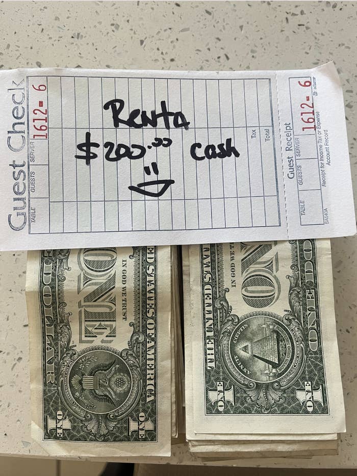 Guest check showing "Renta $200… cash" with a smiley face, placed above stacks of one-dollar bills