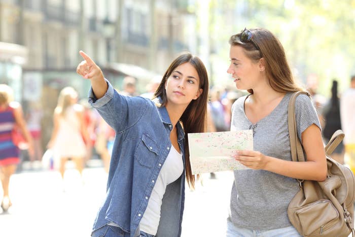 Two women stand in a sunny street, one points ahead while the other consults a map