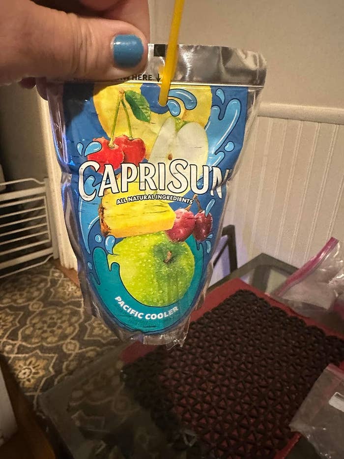 Hand holding a Capri Sun Pacific Cooler juice pouch with a straw inserted