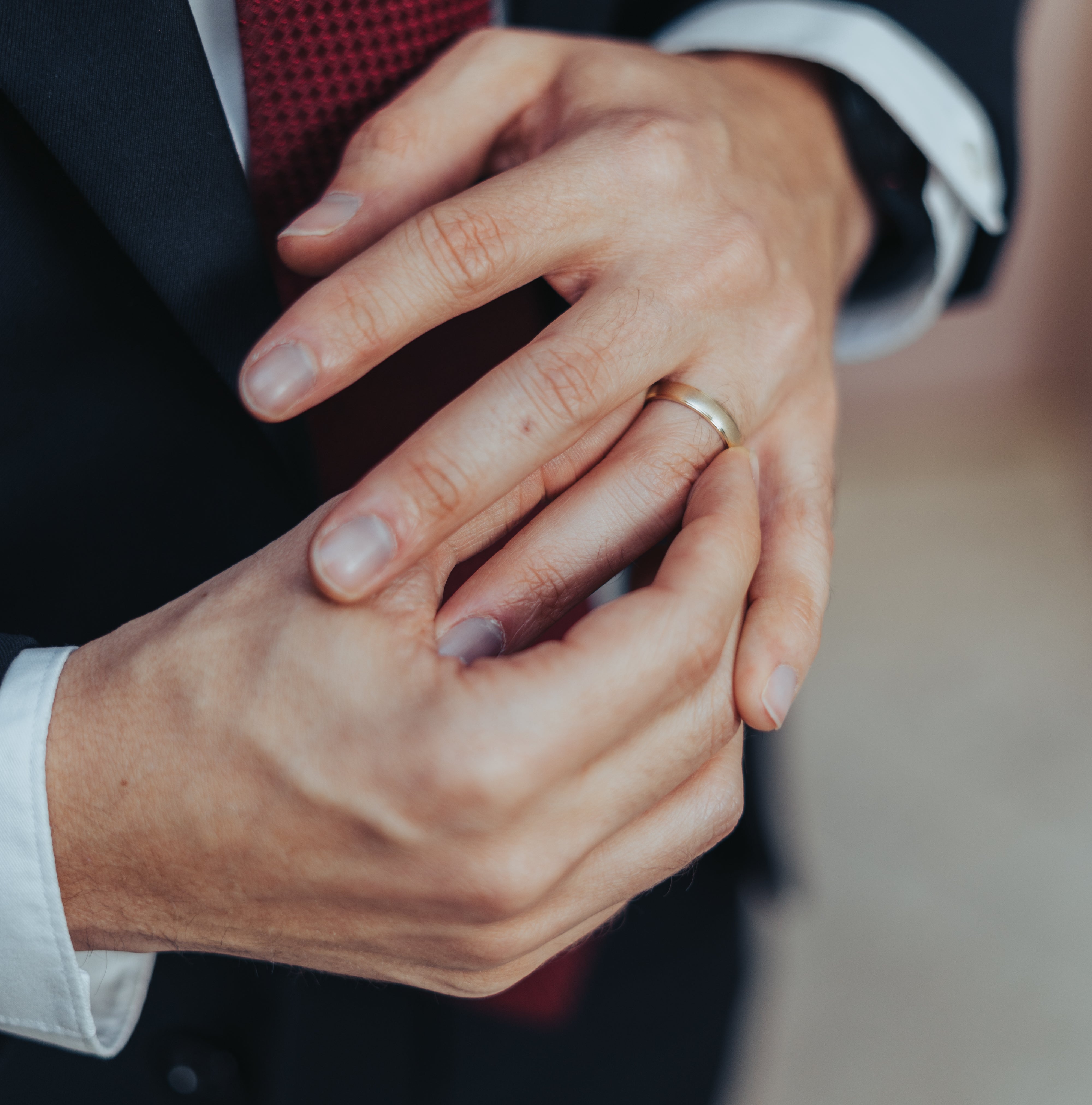 A person in a suit with a red tie is adjusting a gold ring on their left ring finger