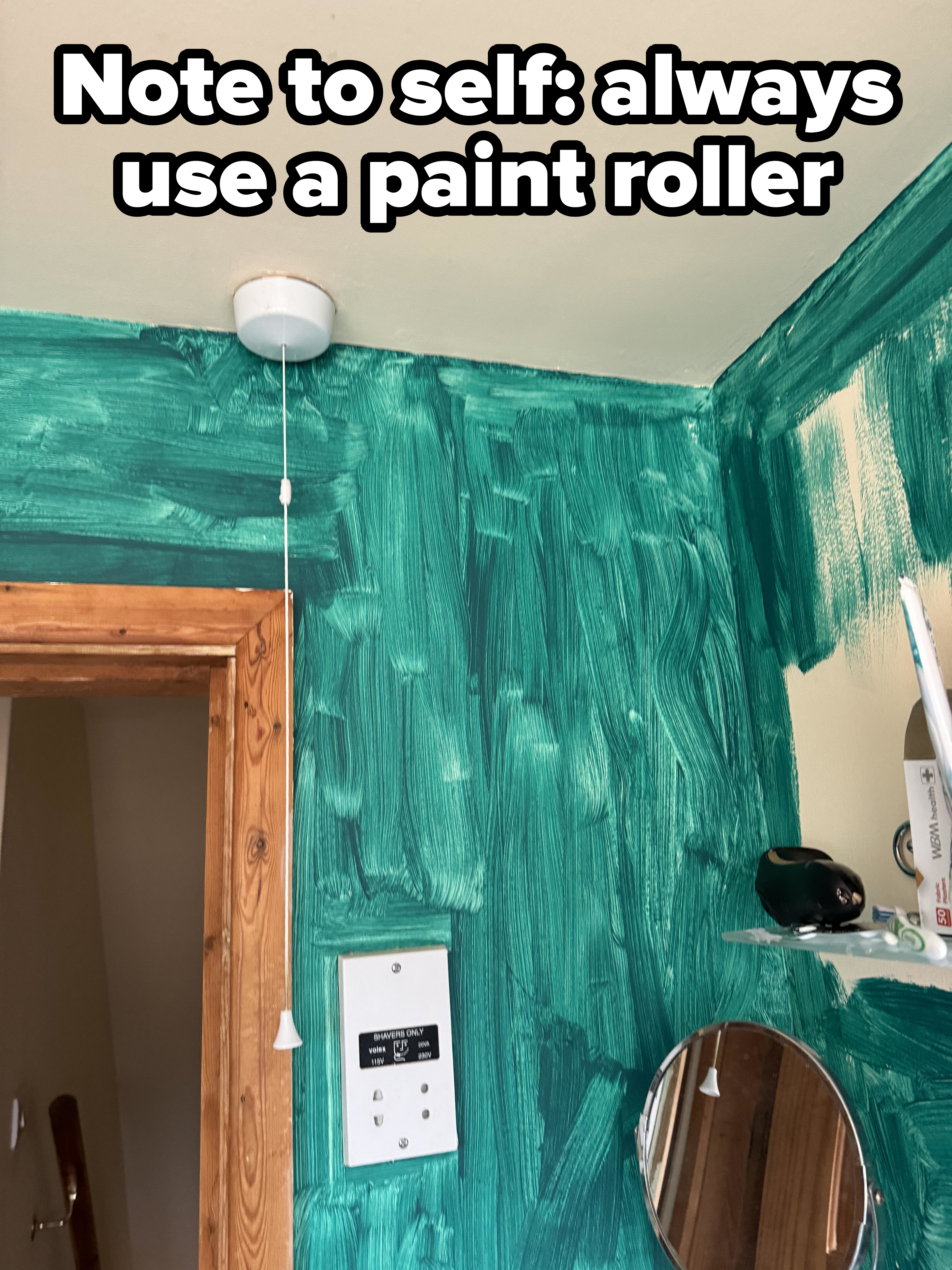 Partially painted room with electric outlets and a mirror. A smoke detector with a pull-cord hangs from the ceiling