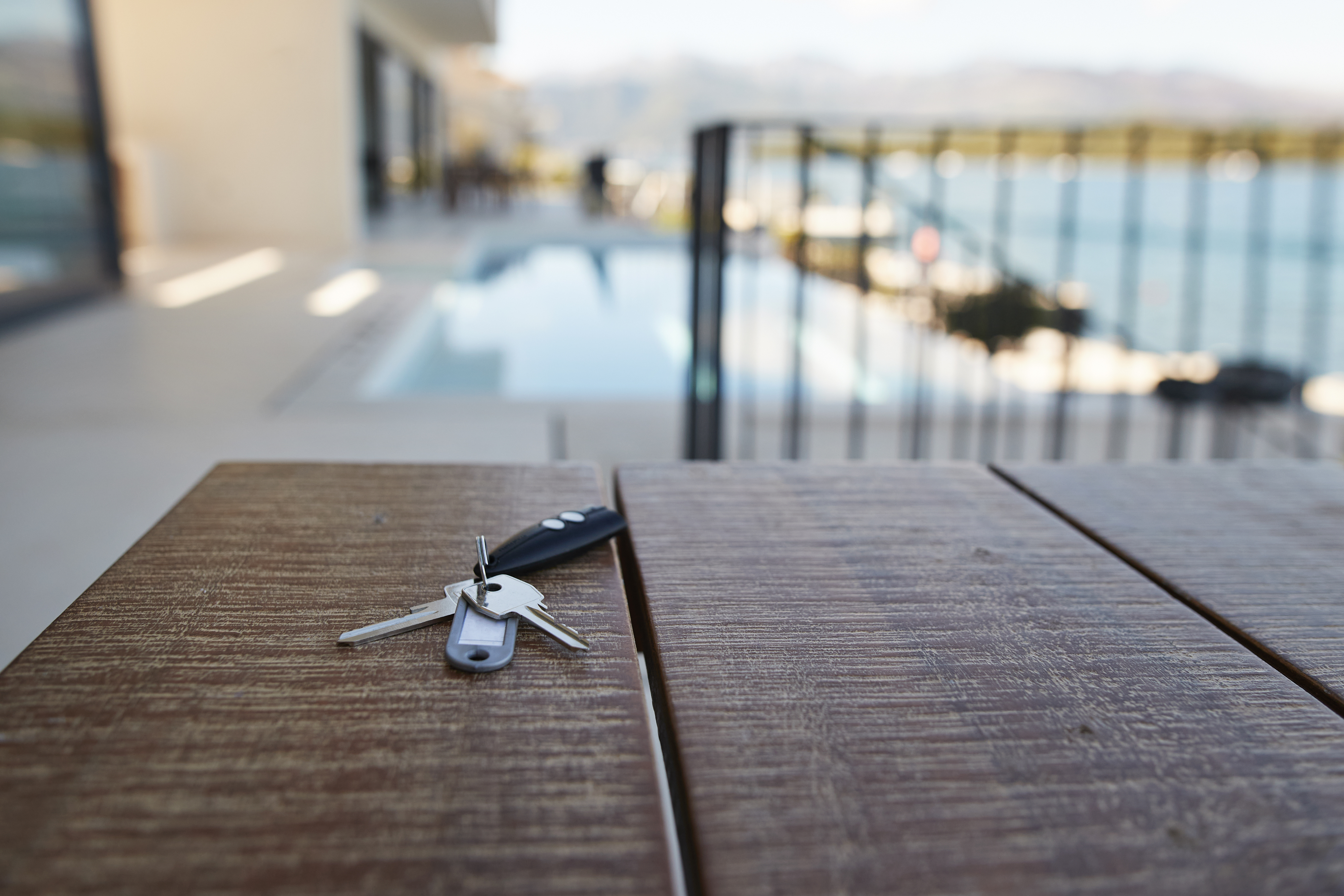 Keys are placed on a wooden table near a pool with a scenic outdoor view