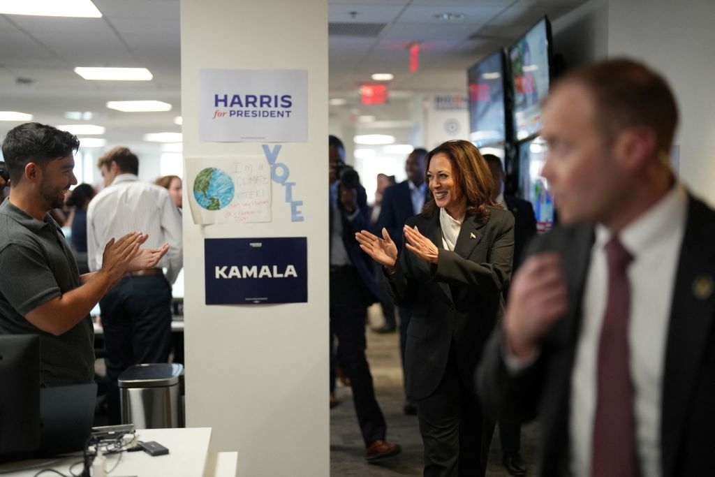 Kamala Harris walks through an office while people applaud. Signs read &quot;Harris for President,&quot; &quot;KAMALA,&quot; and &quot;VOTE.&quot;
