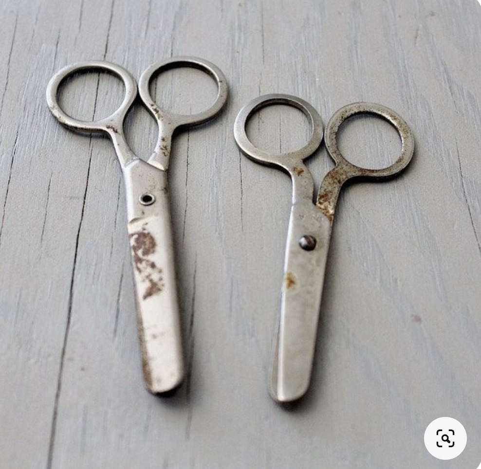 Two vintage metal scissors with wear and rust are placed on a wooden surface, blades closed, resembling the shape of glasses