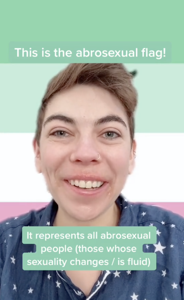 Zoe in a star-patterned shirt smiling. Text reads: "This is the abrosexual flag! It represents all abrosexual people (those whose sexuality changes/is fluid)"