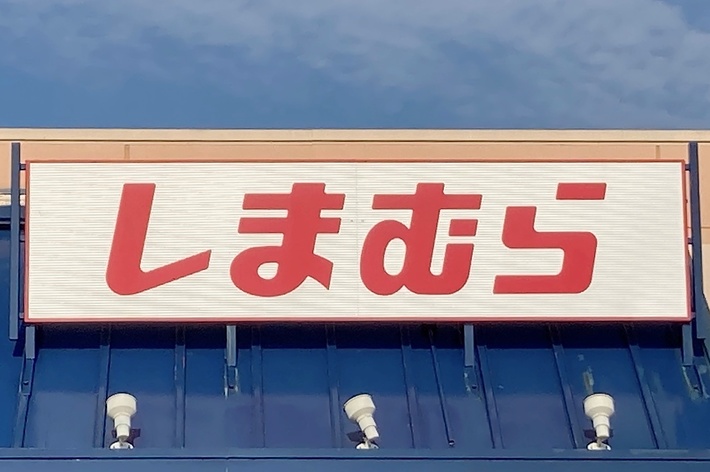 Storefront with a sign in Japanese characters that reads &ldquo;しまむら&rdquo;. The building has an accessible parking sign in front