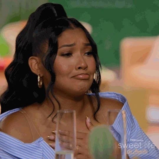 A woman with long, wavy hair and hoop earrings, sits at a table and appears emotional. Text on the image: &quot;sweet life,&quot; a Max Original