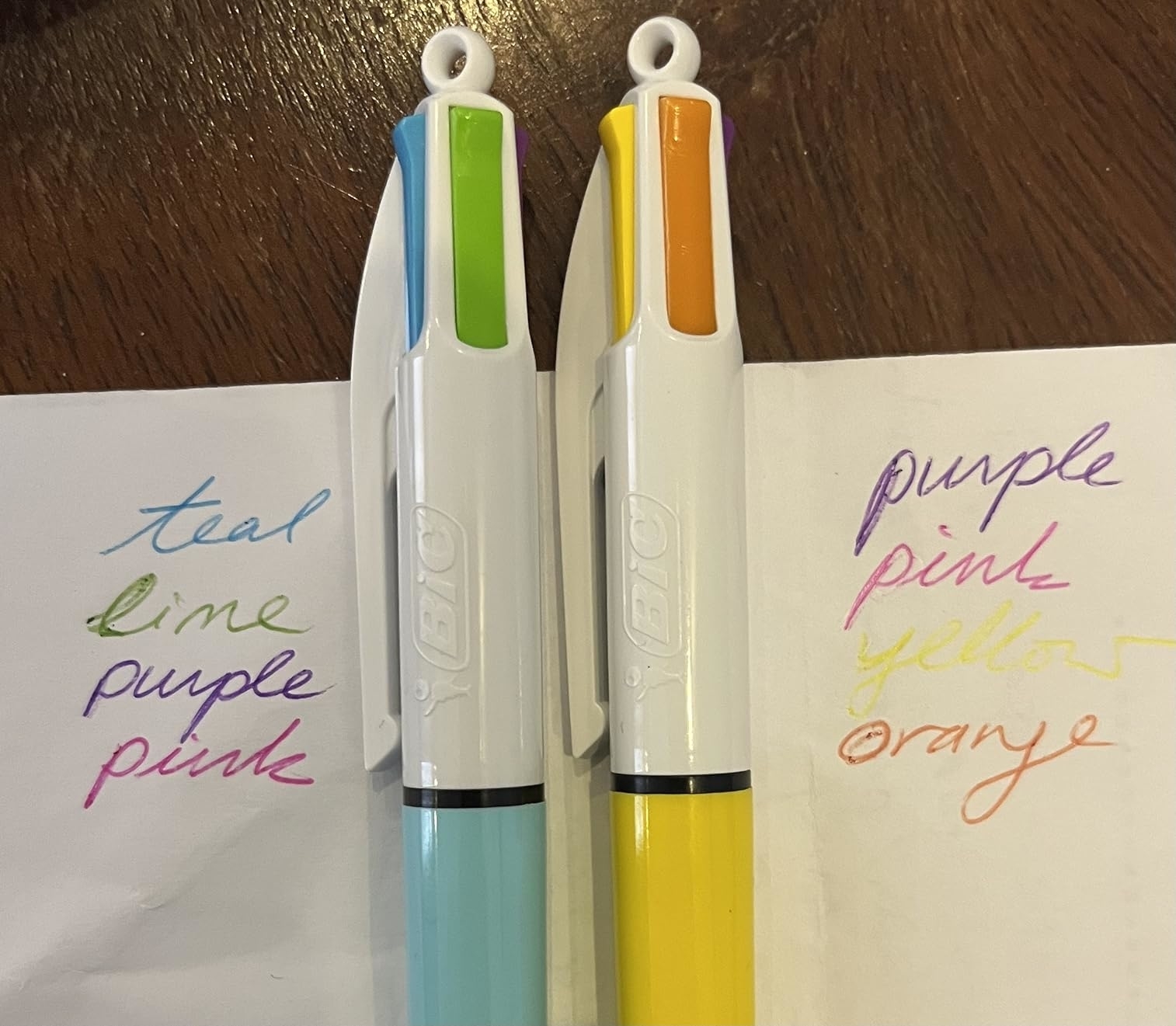 Two multicolor pens with color samples on paper: teal, lime, purple, pink on the left; purple, pink, yellow, orange on the right