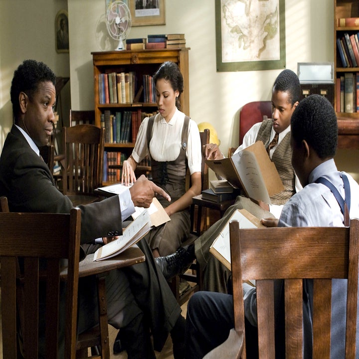 Denzel Washington, Jurnee Smollett-Bell, and two young boys sit at a table in a classroom, focusing on reading books in a serious discussion