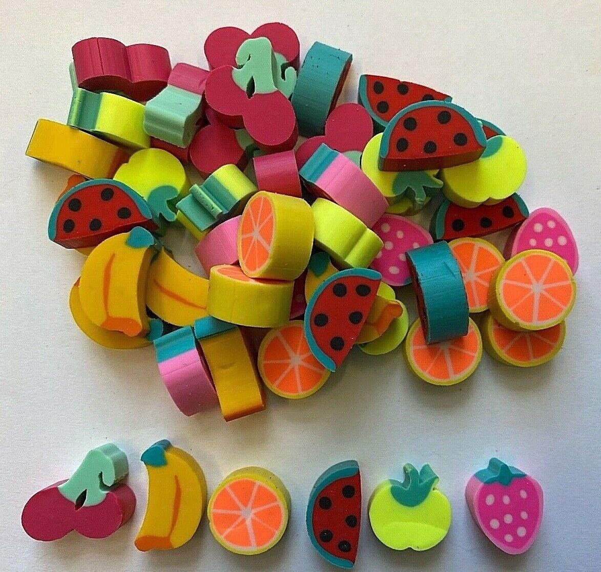 A collection of small, fruit-shaped erasers featuring designs such as watermelon slices, oranges, bananas, strawberries, cherries, and apples