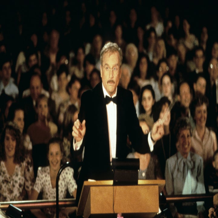 An older man in a tuxedo conducts an orchestra before an audience