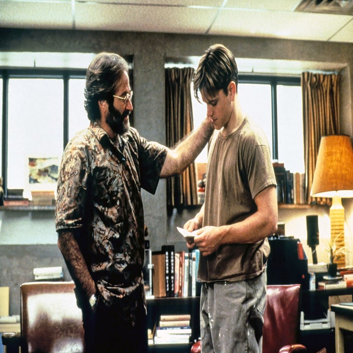 Robin Williams touches Matt Damon's shoulder in a study with vintage furniture. Matt reads a paper, and both are engaged in a serious conversation