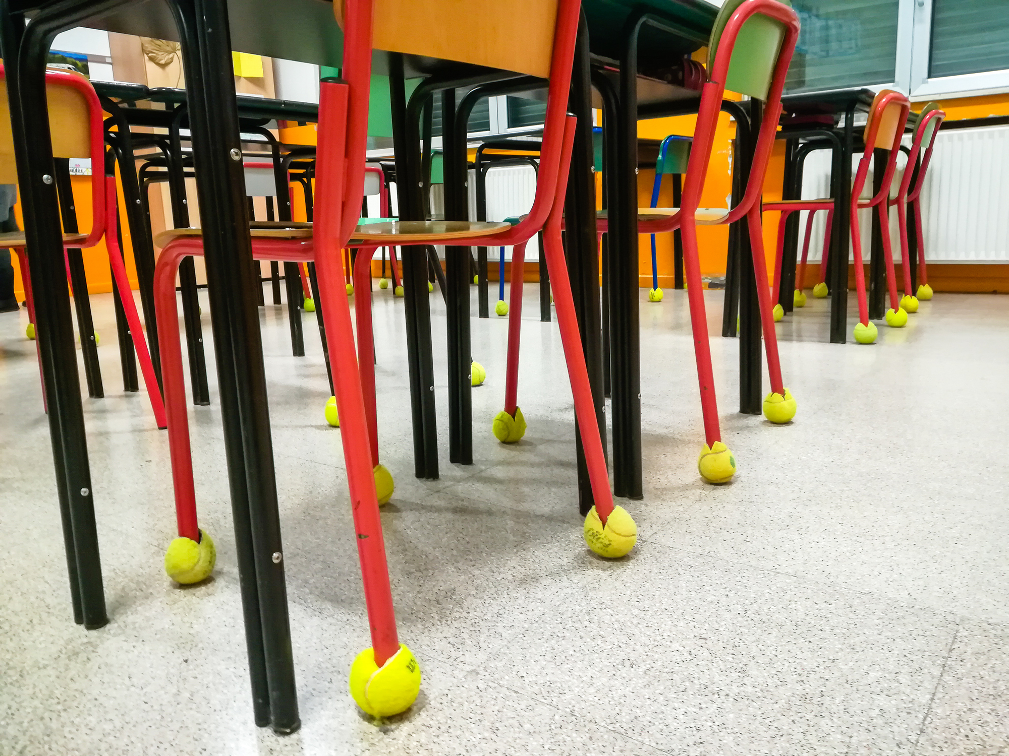 Classroom with chairs placed upside down on desks, each chair leg fitted with a tennis ball