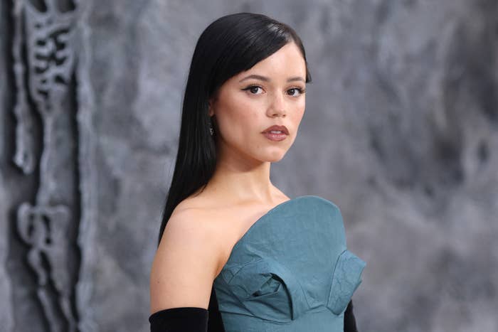 Jenna Ortega is wearing a strapless, sculpted dress and looking towards the camera with a neutral expression at a formal event