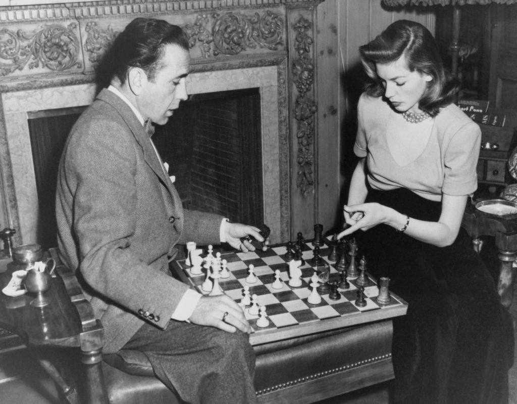 Humphrey Bogart and Lauren Bacall playing chess by a fireplace