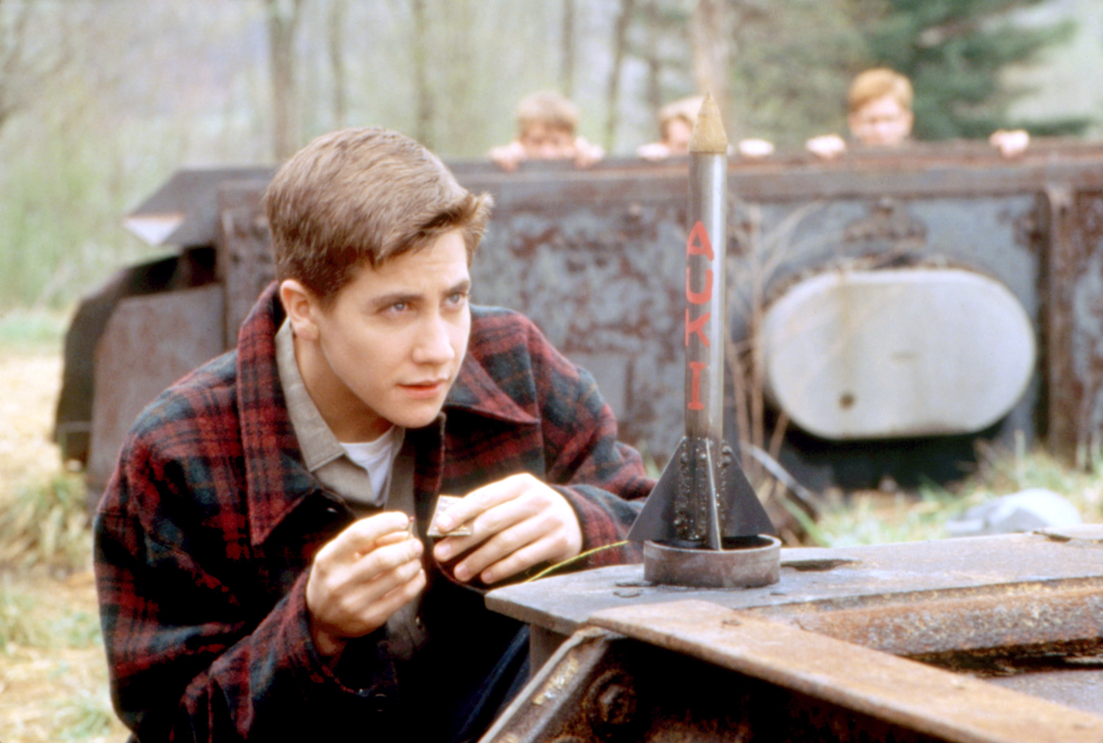 Jake Gyllenhaal in a plaid jacket, carefully prepping a small homemade rocket in a scene from &quot;October Sky.&quot;