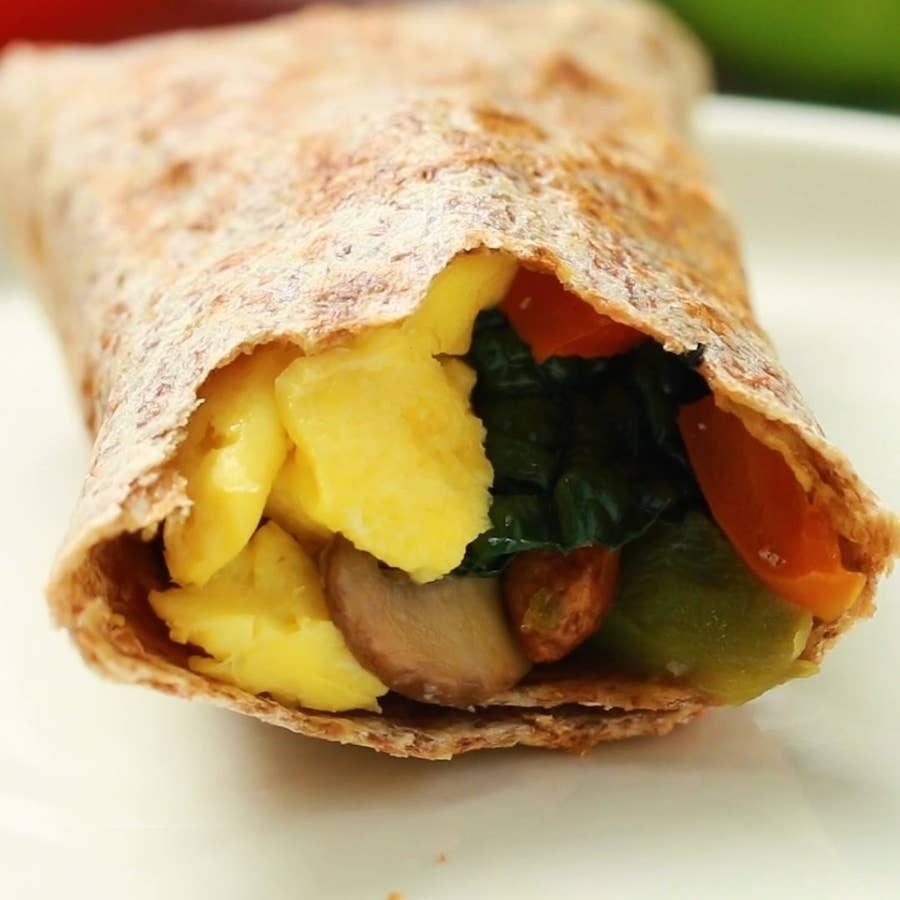Close-up of a breakfast burrito filled with scrambled eggs, mushrooms, bell peppers, and leafy greens