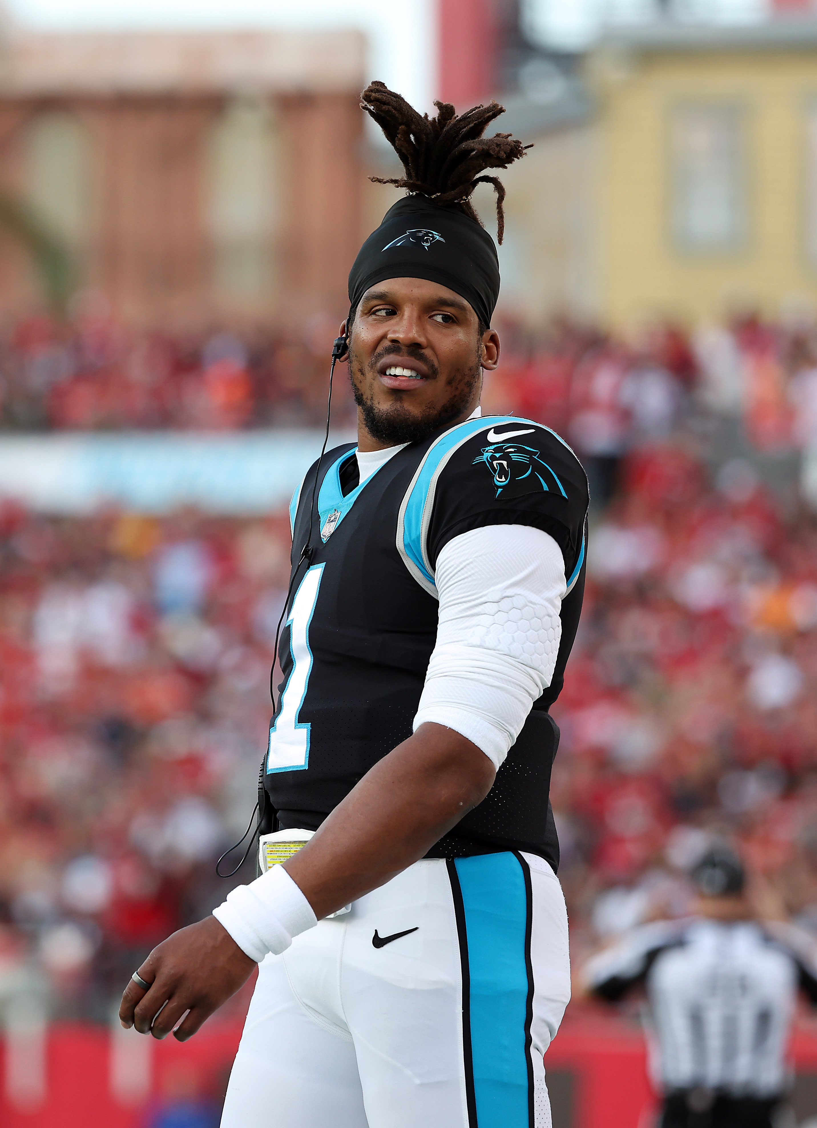 Cam Newton, wearing a football uniform with the number 1, smiles on the field during a game