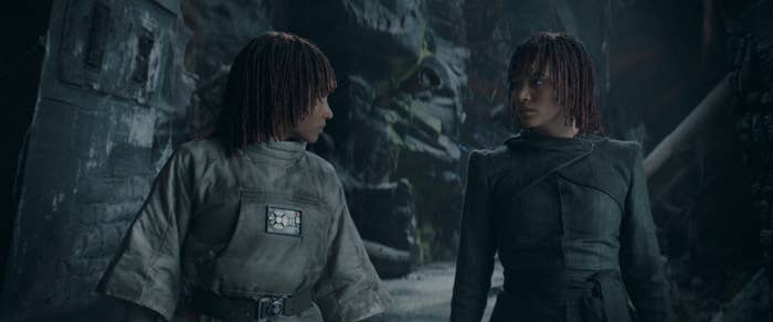 Osha and Mae in contrasting rugged outfits, in a dim, rocky environment