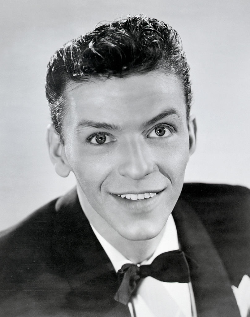 A man in a tuxedo with a bow tie smiles directly at the camera