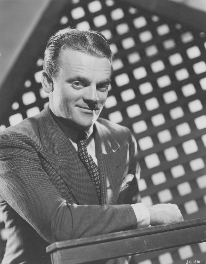 A man in a suit with a patterned tie, posing for a professional portrait with a grid-patterned backdrop