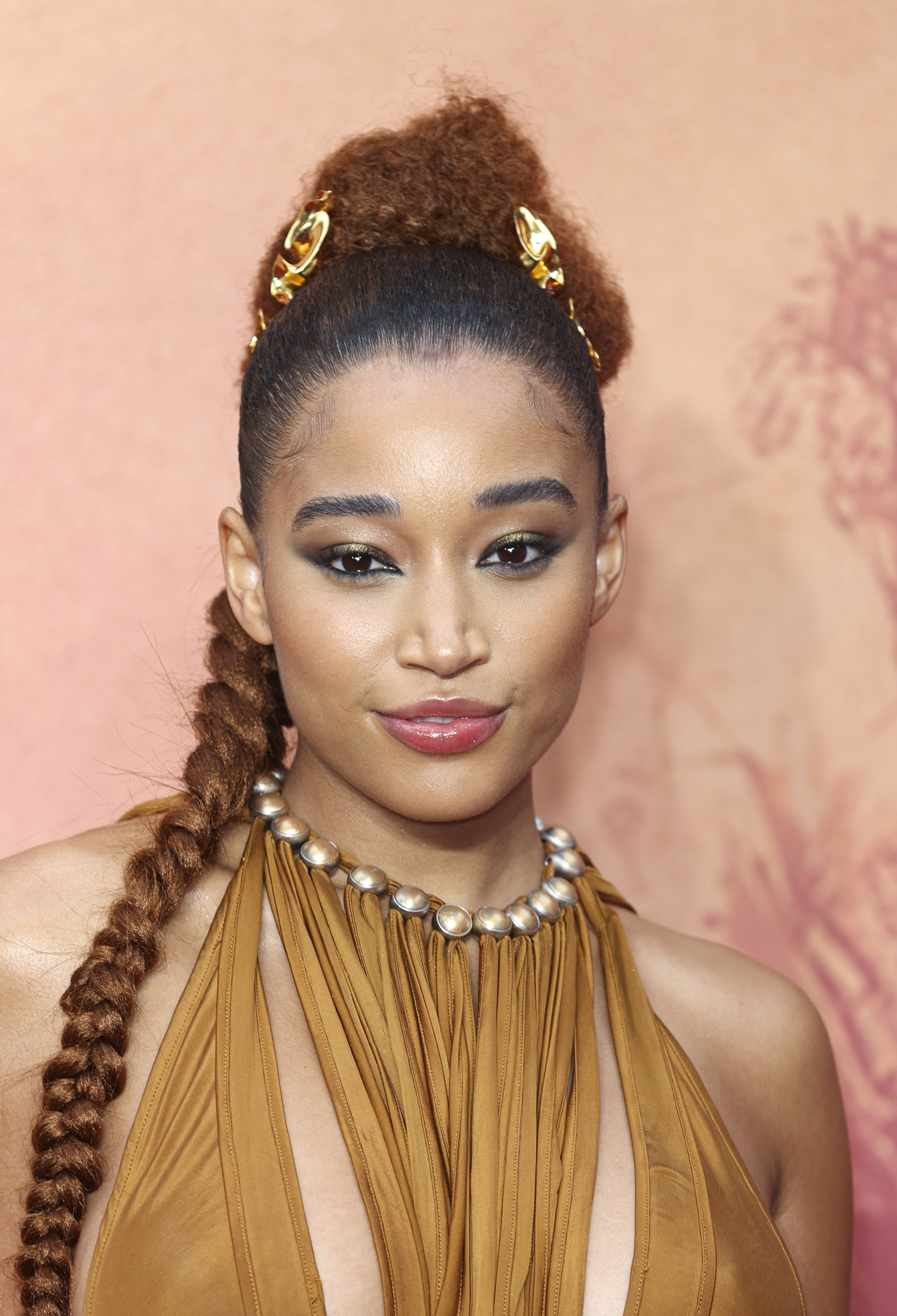Amandla Stenberg wearing a stylish halterneck dress and sporting a long braided hairstyle with gold accessories on the red carpet