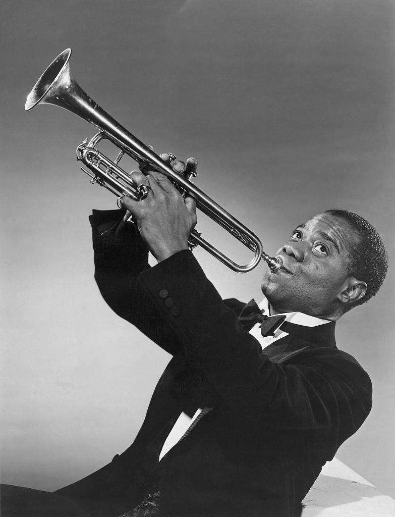 Louis Armstrong plays the trumpet, wearing a tuxedo with a bow tie, looking to his left