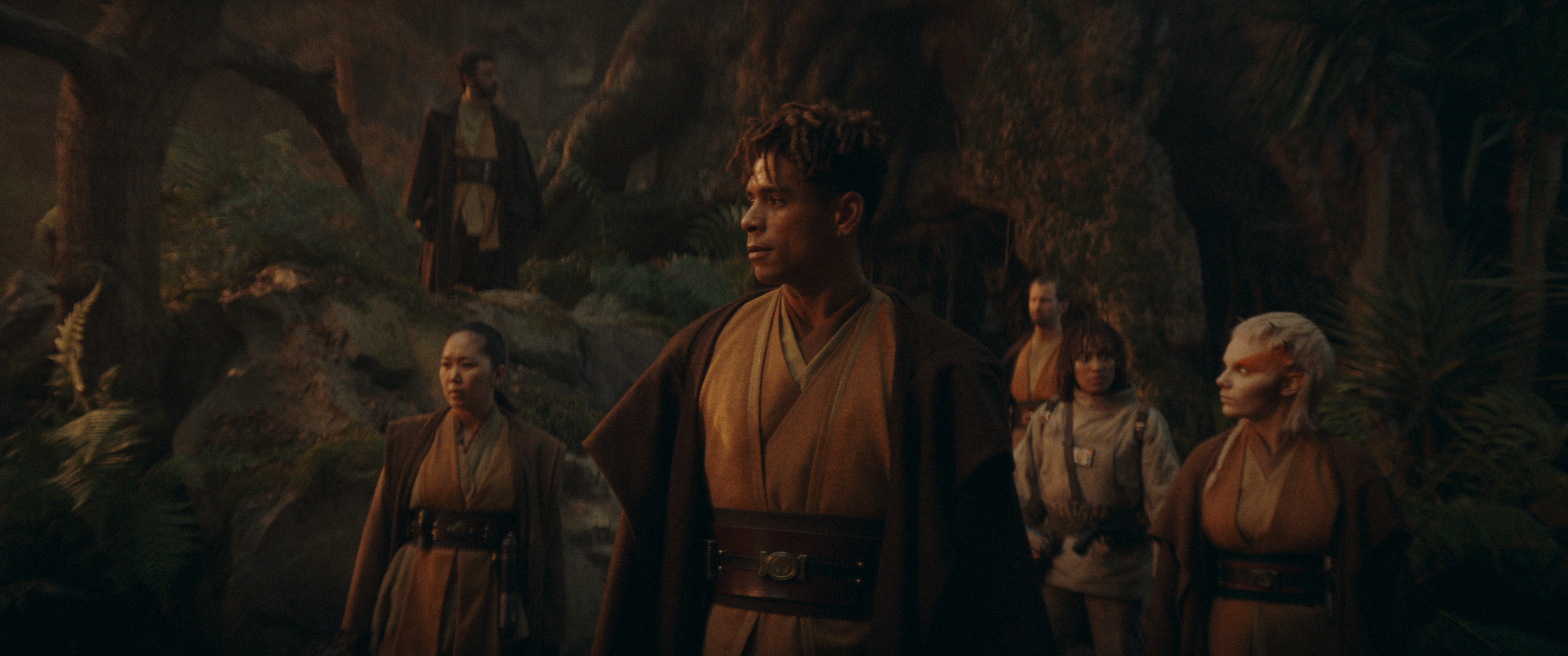 A group of Jedi, including Reva Sevander, Cal Kestis, Merrin, and two others, stands in a forest, wearing traditional Jedi robes as they look around cautiously
