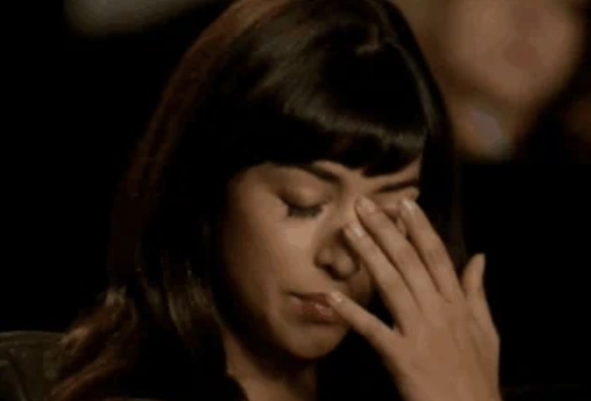 A woman with long hair and bangs, looking distressed, covers her face with her hand