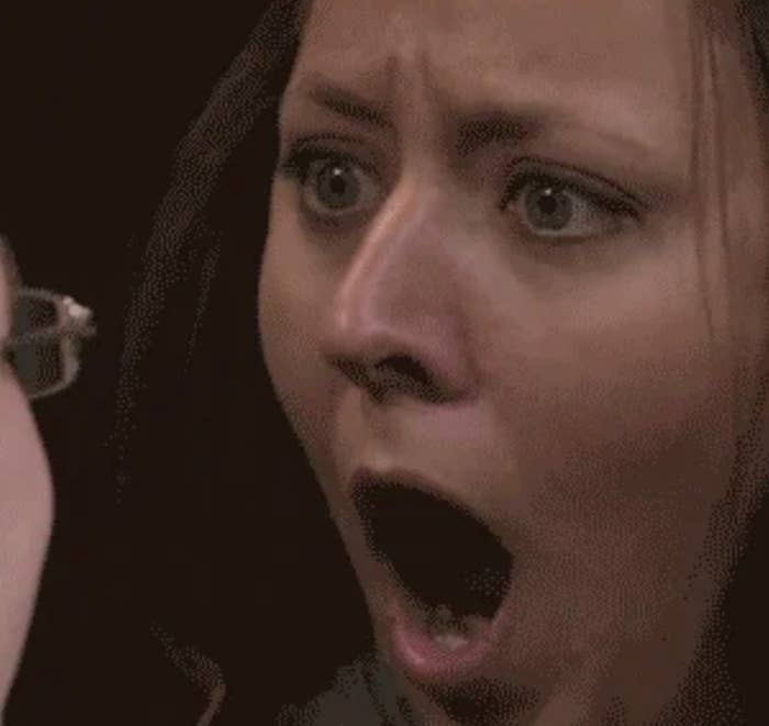 A woman looks shocked, mouth wide open, facing another person who is partially out of the frame