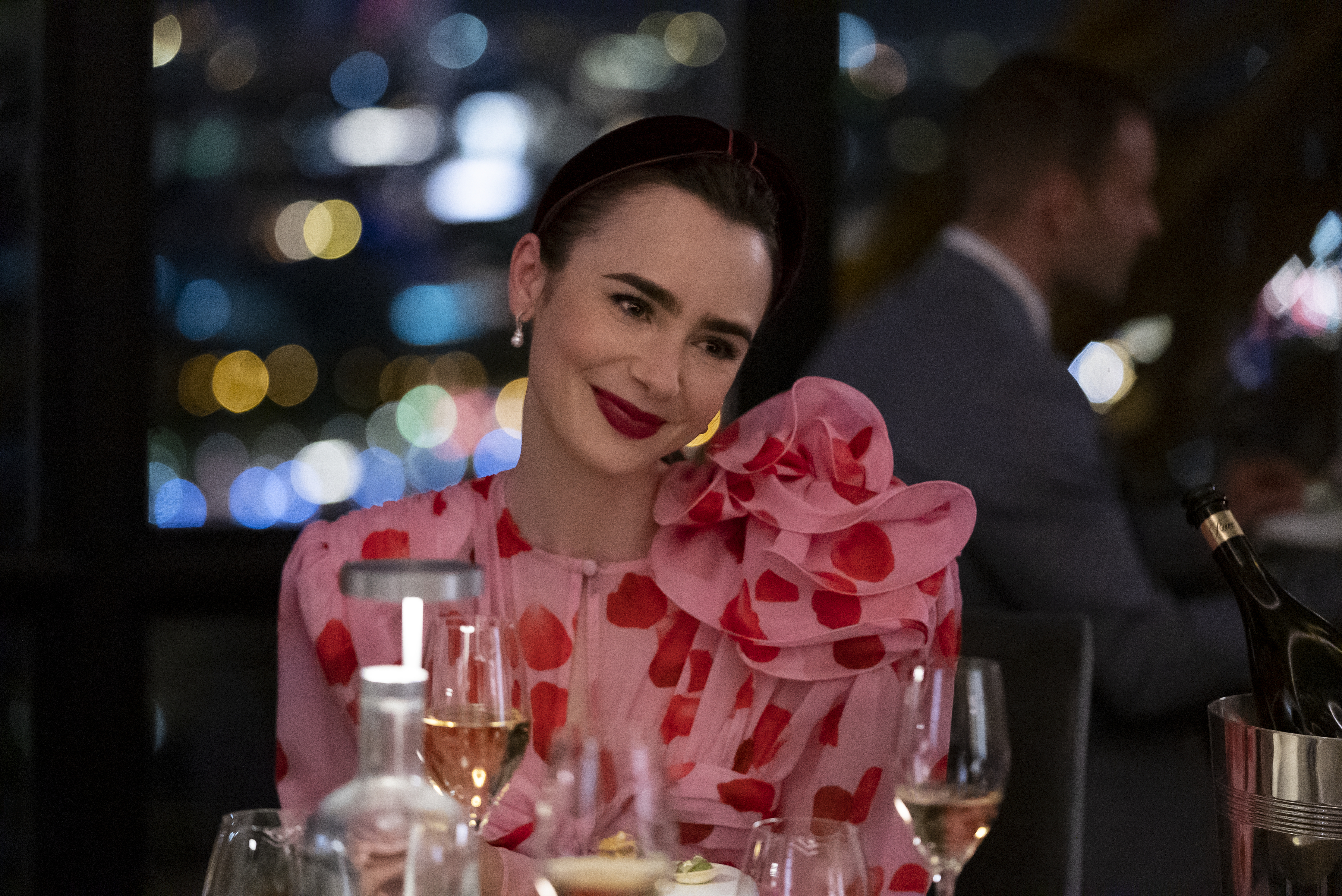 Lily Collins in a chic, ruffled blouse with red patterns, dining at a restaurant in "Emily in Paris."