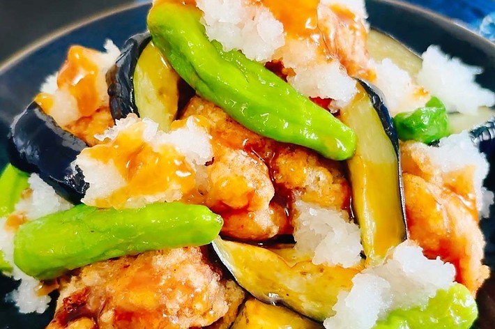 野菜と揚げた肉が混ざった料理の拡大写真。鮮やかなピーマンやナスが見える。