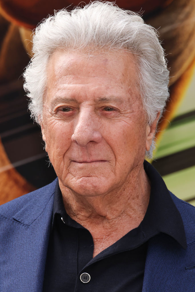 Dustin Hoffman at a public event, wearing a black shirt beneath a blue jacket