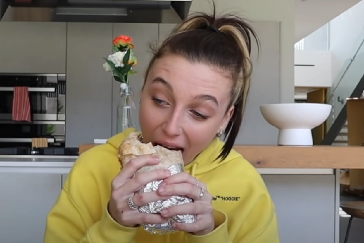 Emma Chamberlain taking a bite of a foil-wrapped burrito