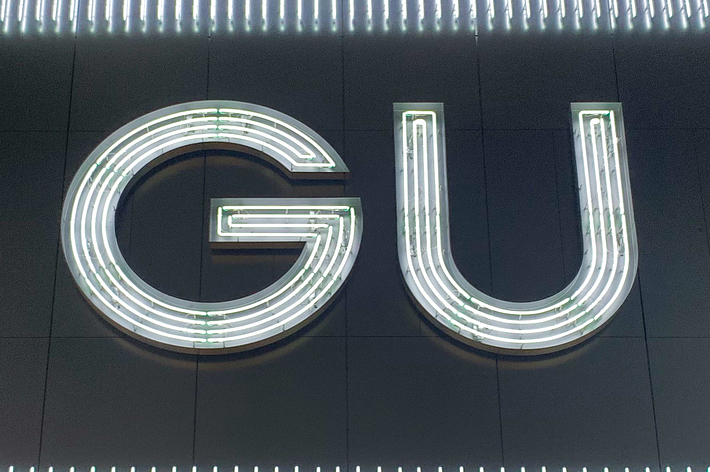 A large neon sign displaying the letters &ldquo;GU&rdquo; in a bold, sans-serif font, with horizontal lights surrounding it