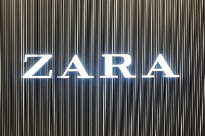 The image displays a wall with vertical lines and the illuminated text “ZARA” in the center