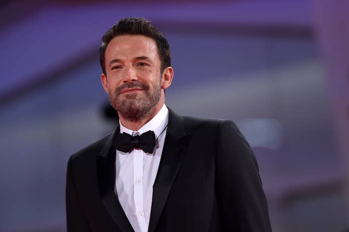 Ben Affleck on a red carpet, wearing a classic black tuxedo. He is smiling and looking to the side