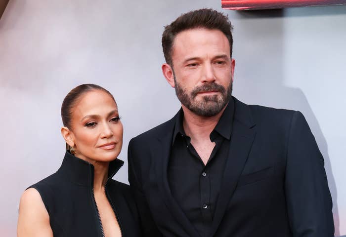 Jennifer Lopez and Ben Affleck on the red carpet; Jennifer wearing a high-neck black outfit, Ben in a black suit, both with neutral expressions