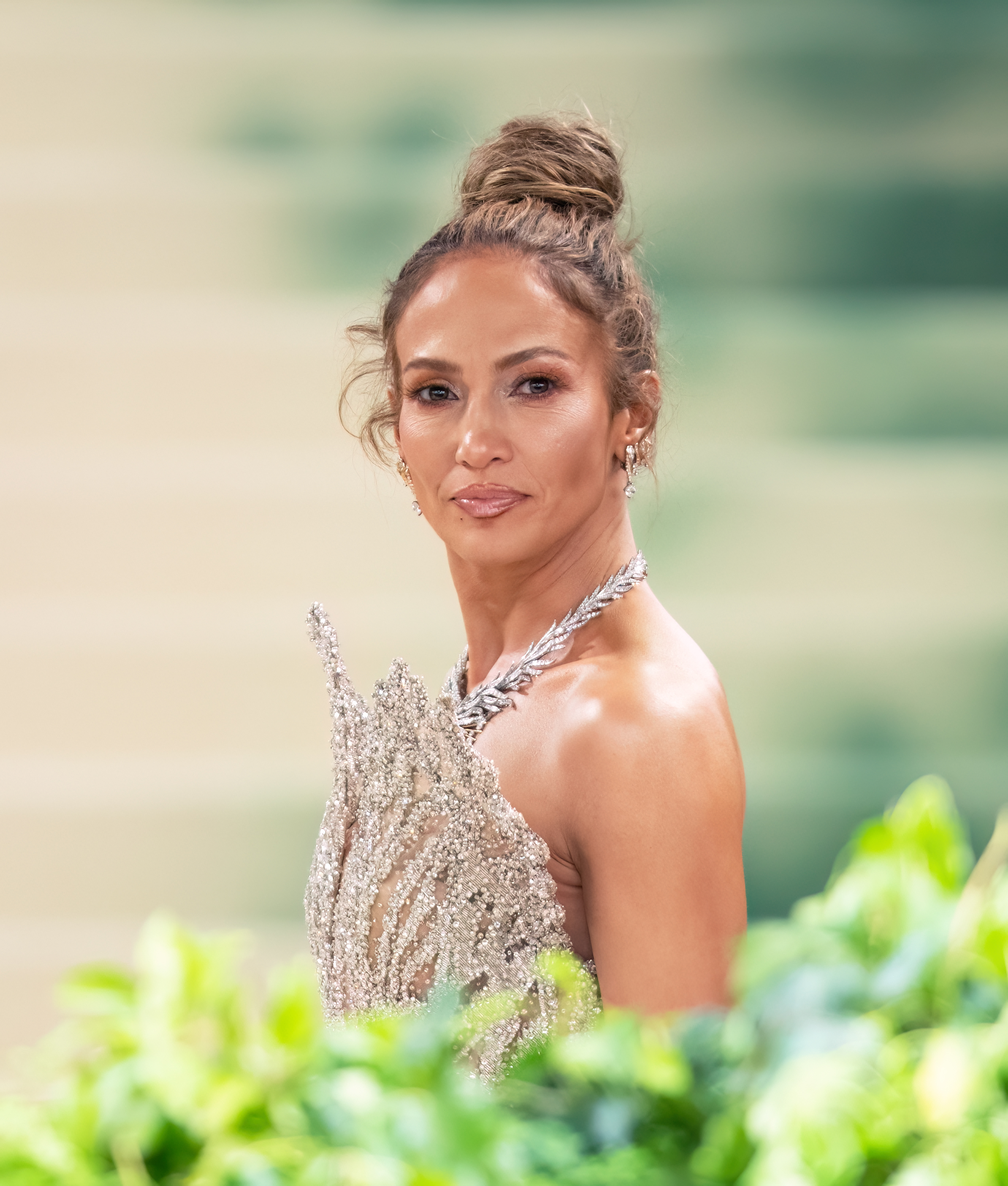 Jennifer Lopez poses on the red carpet wearing an elegant dress with intricate detailing and a high bun hairstyle
